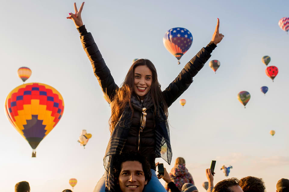 Woman with arms raised at a hot air balloon launch.